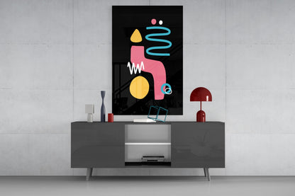 Abstract colorful glass wall art with pink, yellow, and cyan geometric shapes displayed above a gray media console in a modern interior setting.