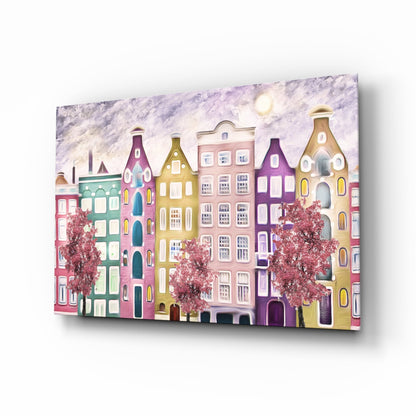 Angled perspective view of colorful glass wall art depicting a whimsical row of pastel buildings with distinctive peaked roofs, flowering trees, and moonlit sky.