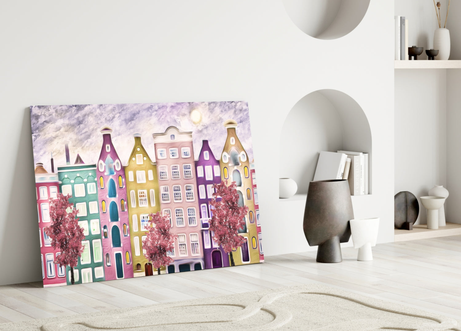 Colorful glass wall art depicting whimsical multi-story buildings in pink, purple, and gold leaning against white interior wall with shelving.