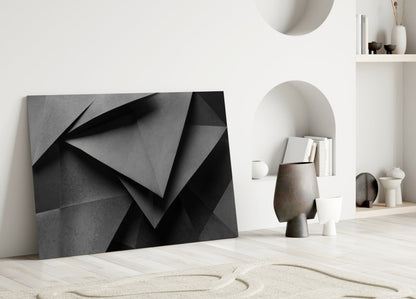Modern minimalist interior showroom featuring black geometric glass wall art leaning against white wall beside neutral decorative objects.