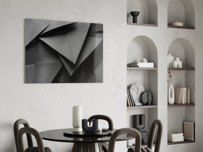 Monochromatic geometric abstract wall art with folded paper shapes displayed above a round black dining table in a minimalist interior.