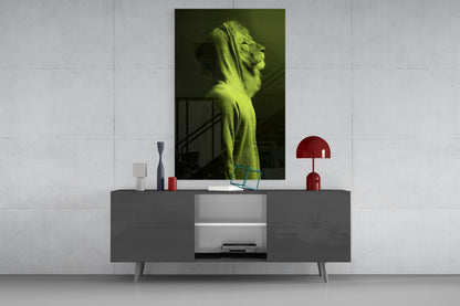 Green lion head glass wall art displayed above gray sideboard with red lamp and decorative accessories in modern interior setting.