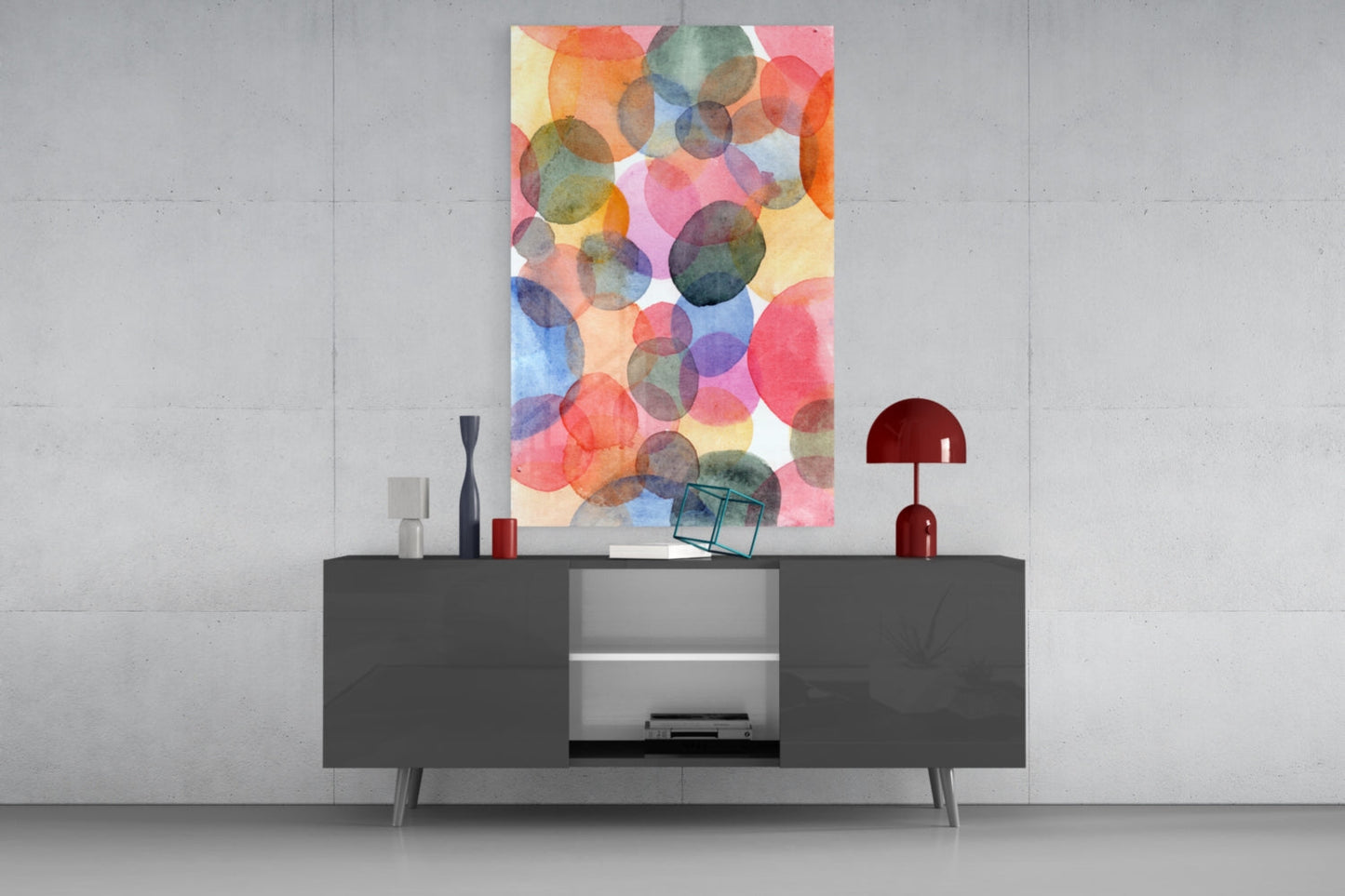 Colorful abstract watercolor glass wall art with overlapping translucent circles in red, orange, yellow, blue, and green tones displayed above a dark gray sideboard.