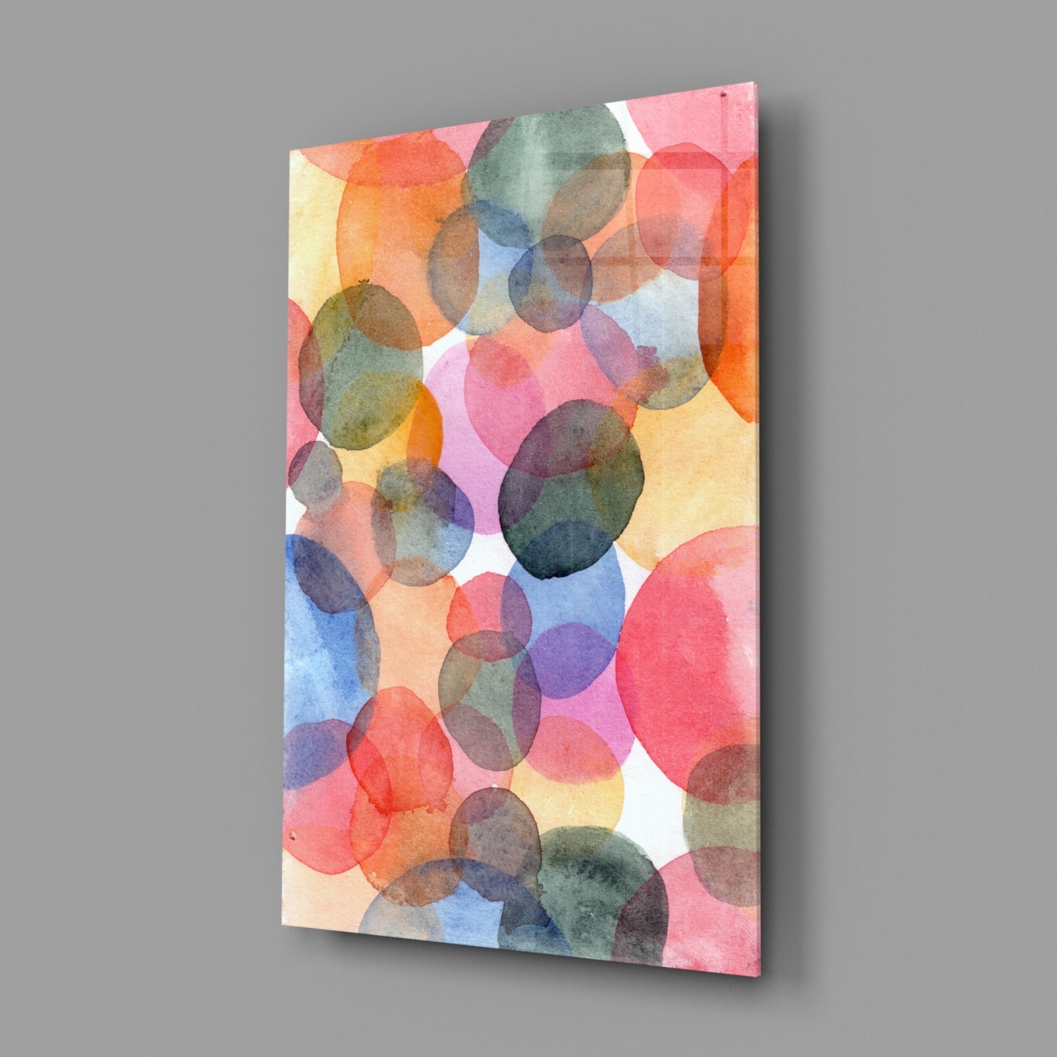 Angled view of rectangular glass wall art displaying overlapping watercolor circles in pink, orange, blue, yellow, and green on white background.