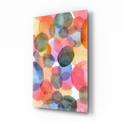 Angled view of a rectangular glass wall art panel featuring overlapping watercolor circles in pink, orange, blue, yellow, and green tones on a light background.