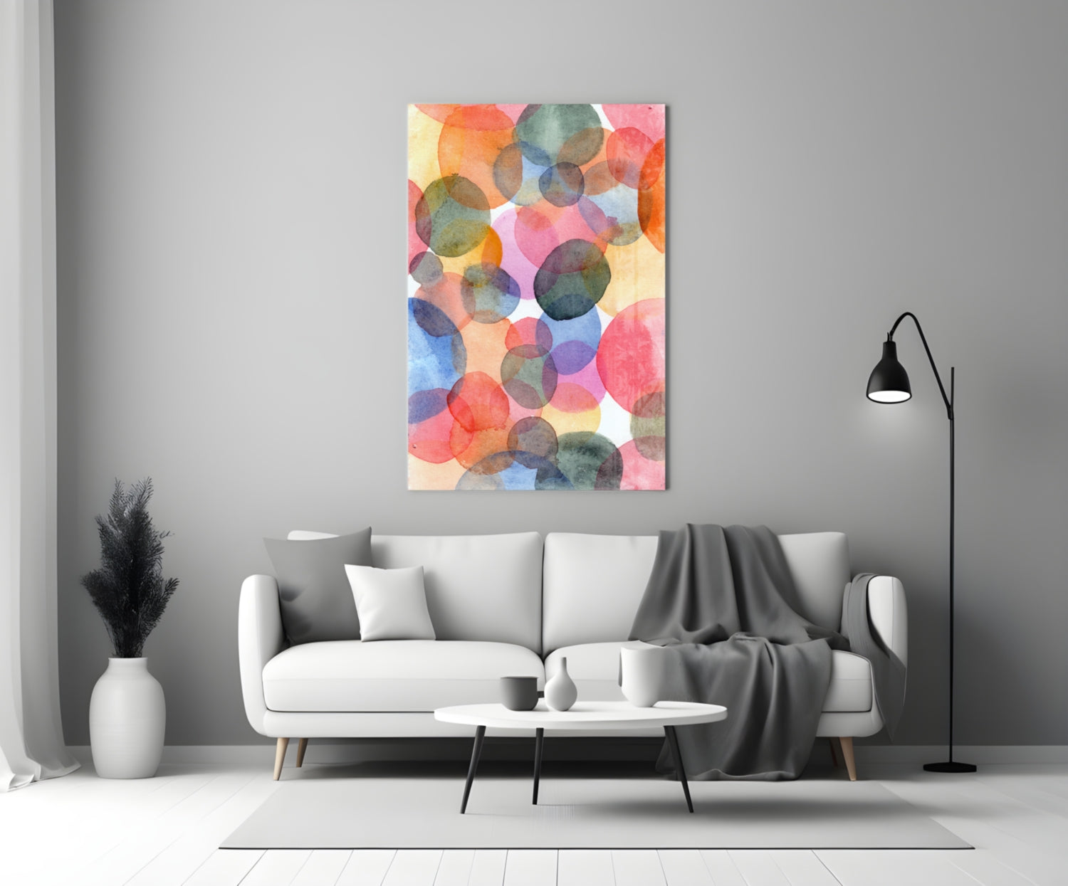 Colorful watercolor glass wall art with overlapping translucent circles in red, pink, blue, and green hung above a white sofa in a modern living room.