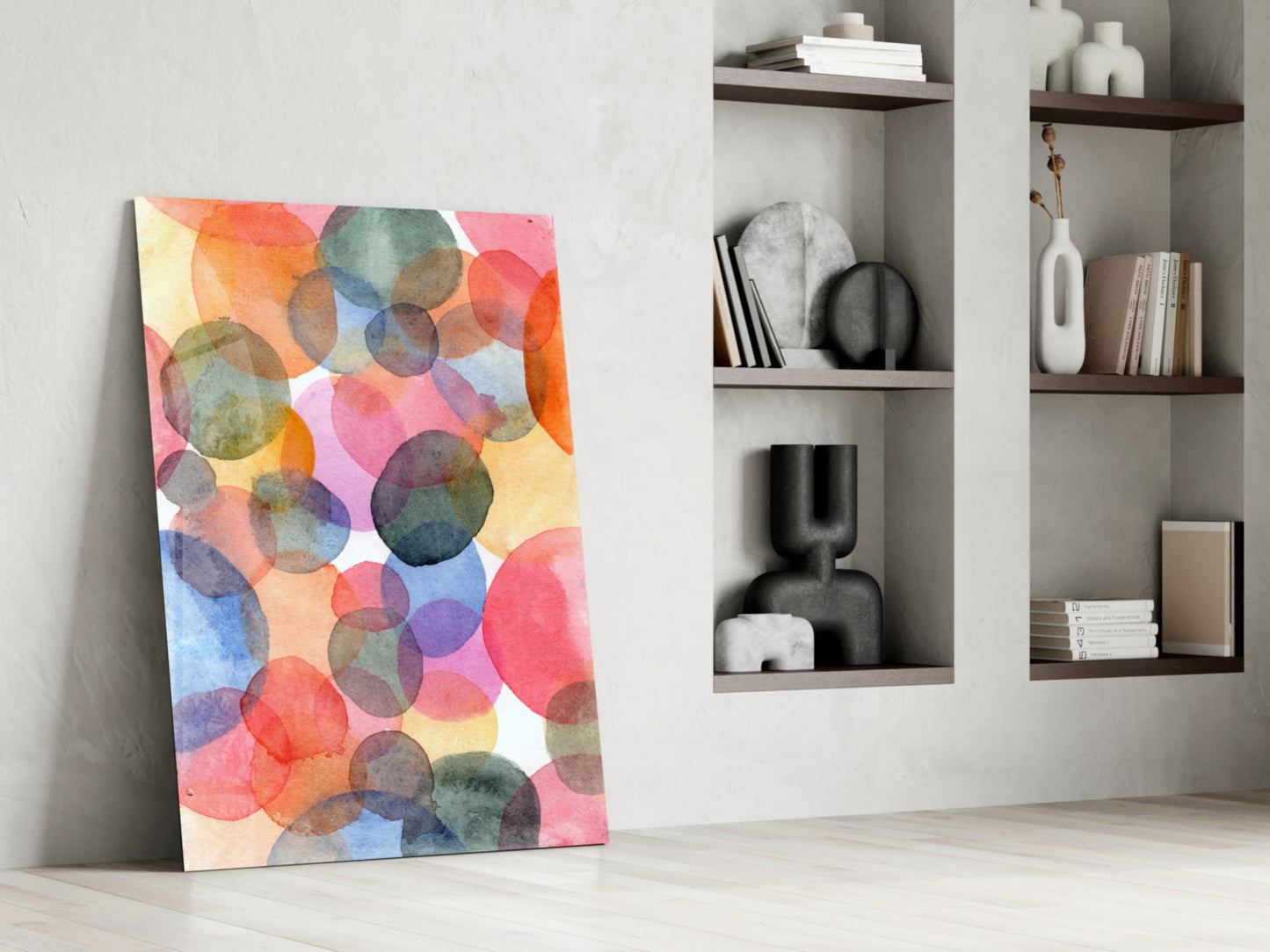 Colorful watercolor glass wall art with overlapping translucent circles in pink, orange, blue, and yellow tones leaning against white wall beside shelving.