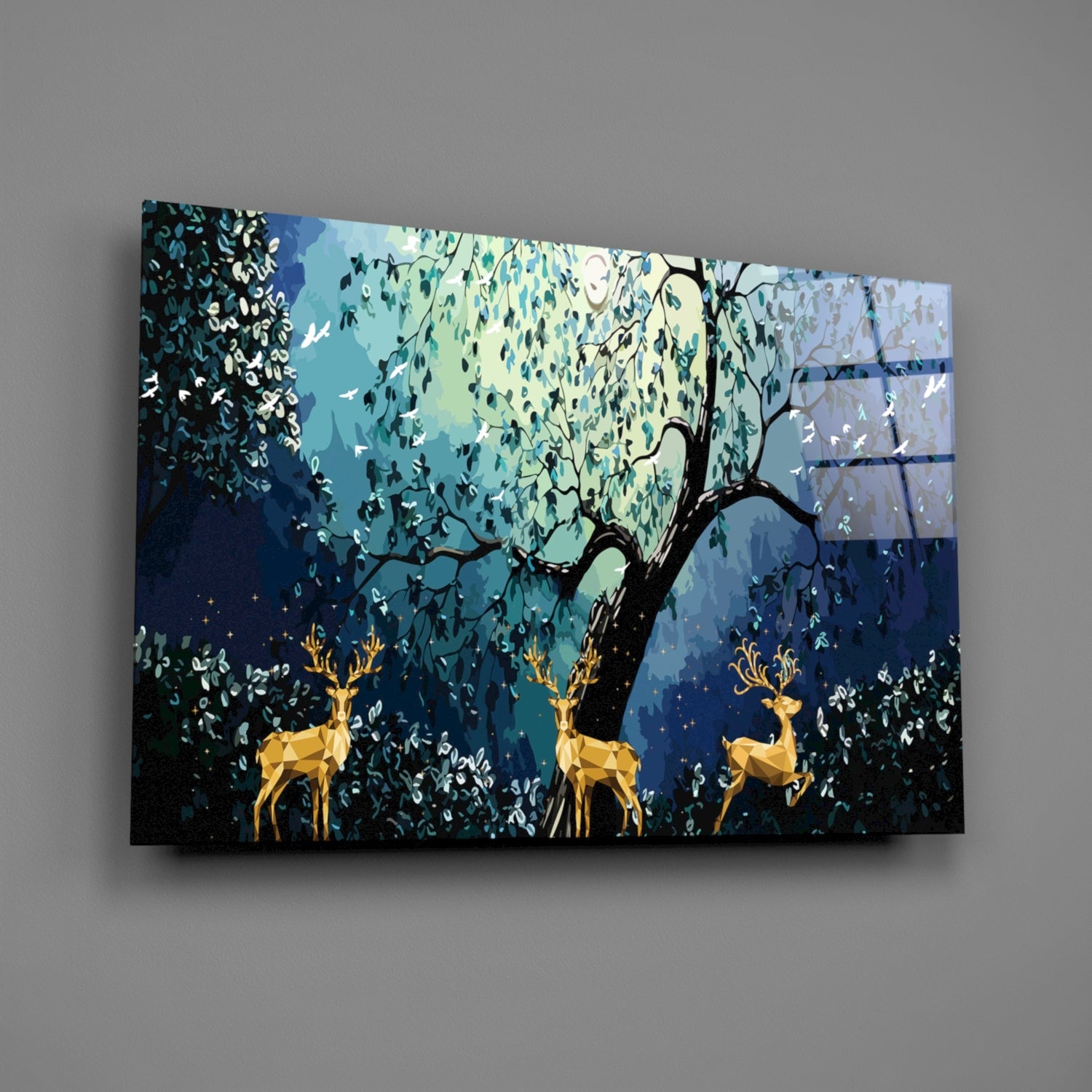 Angled view of glass wall art featuring golden geometric deer beneath a dark tree with hanging foliage against blue and green layered background.