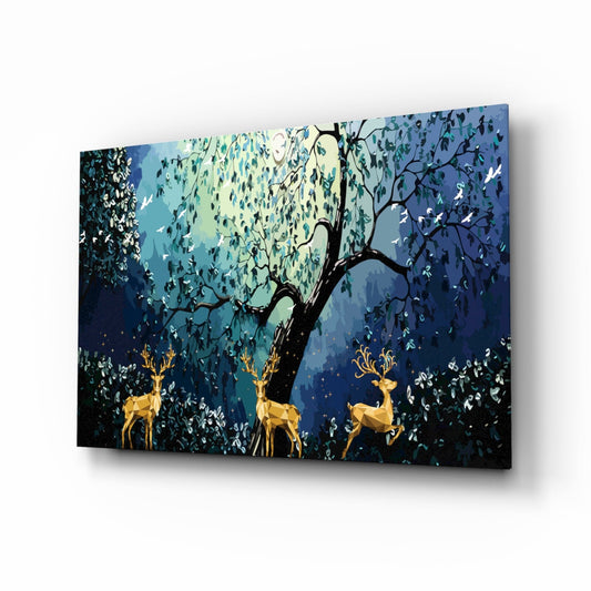 Angled perspective of glass wall art featuring three golden deer beneath a dark tree with blue-green foliage and white birds against a layered blue background.