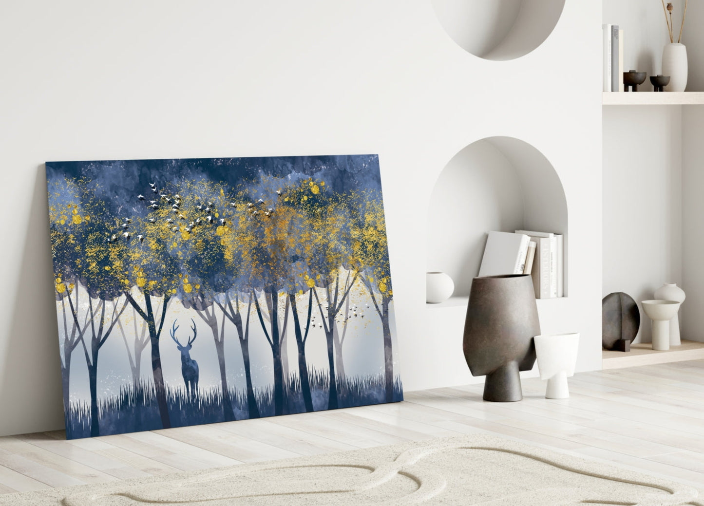 Glass wall art leaning against white wall displays deer in forest with golden yellow foliage and blue tones.