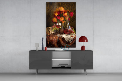 Glass wall art featuring vibrant orange and red flowers in vase with wine bottle and grapes, displayed above modern gray console table.