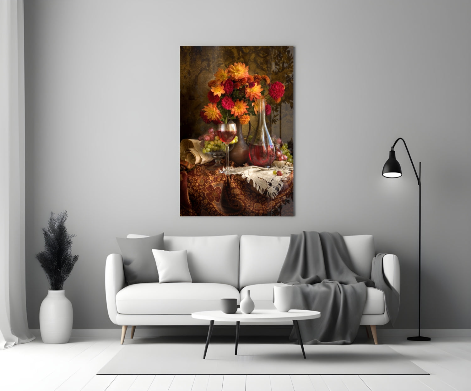 Floral still life glass wall art displaying red and yellow flowers in a vase with wine bottle and glass, hung above a white sofa in a minimalist living room.