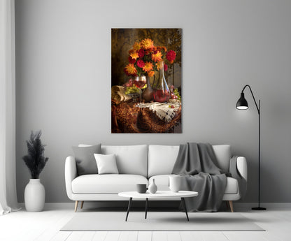 Floral still life glass wall art displaying red and yellow flowers in a vase with wine bottle and glass, hung above a white sofa in a minimalist living room.