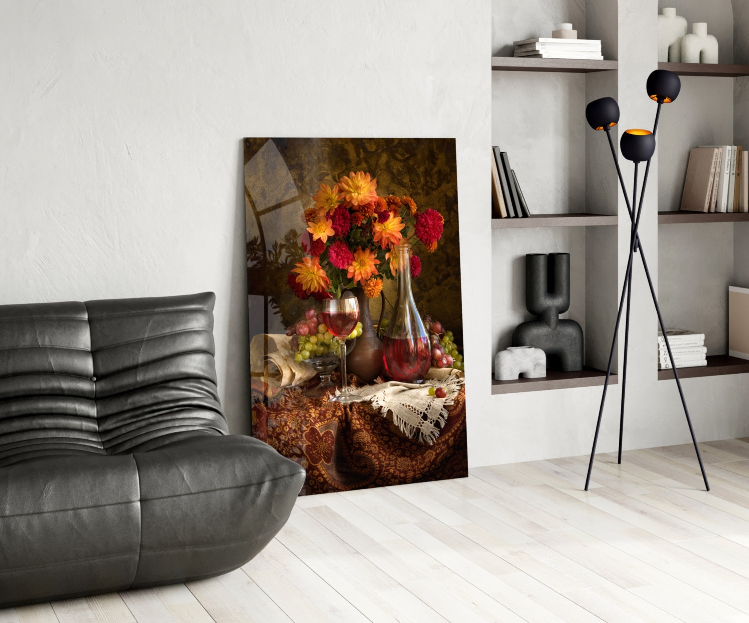 Glass wall art depicting red and yellow flowers in vases with wine glasses and fruit on draped fabric, displayed in modern living room setting.