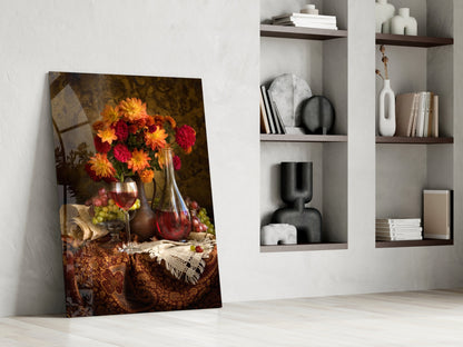 Glass wall art leaning against white wall displays vibrant red and yellow flowers with wine bottles and fruit in warm, classical still-life composition.