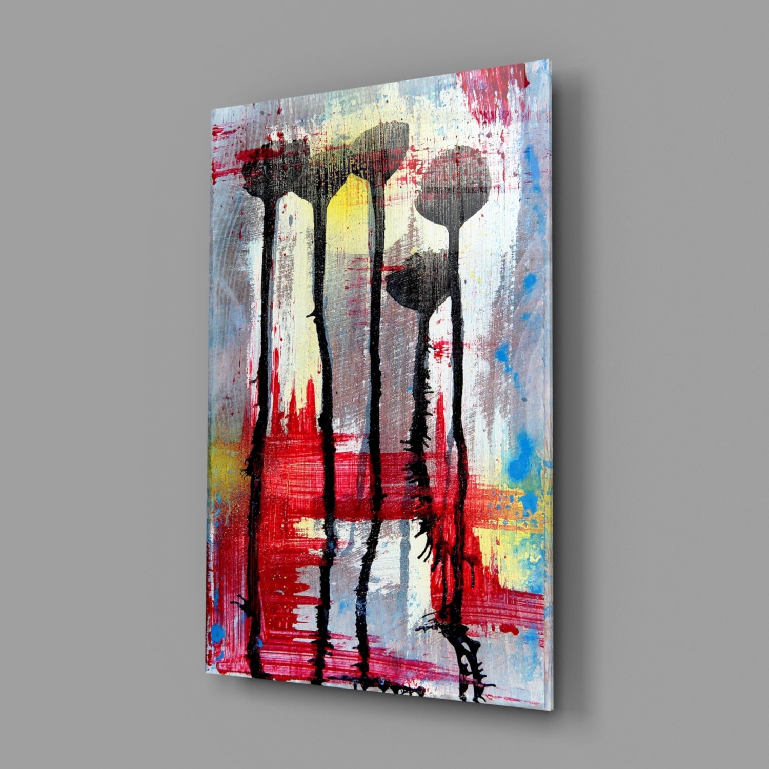 Angled view of glass wall art with four black flower silhouettes against red, white, yellow, and blue painted background.
