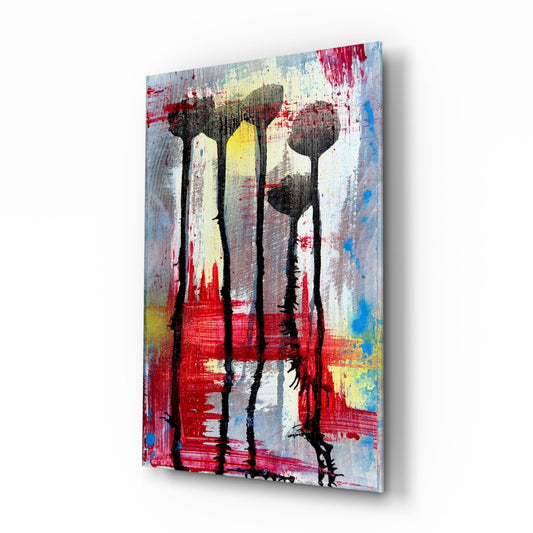Angled view of glass wall art featuring four black flower silhouettes against red, yellow, blue, and white painted background.
