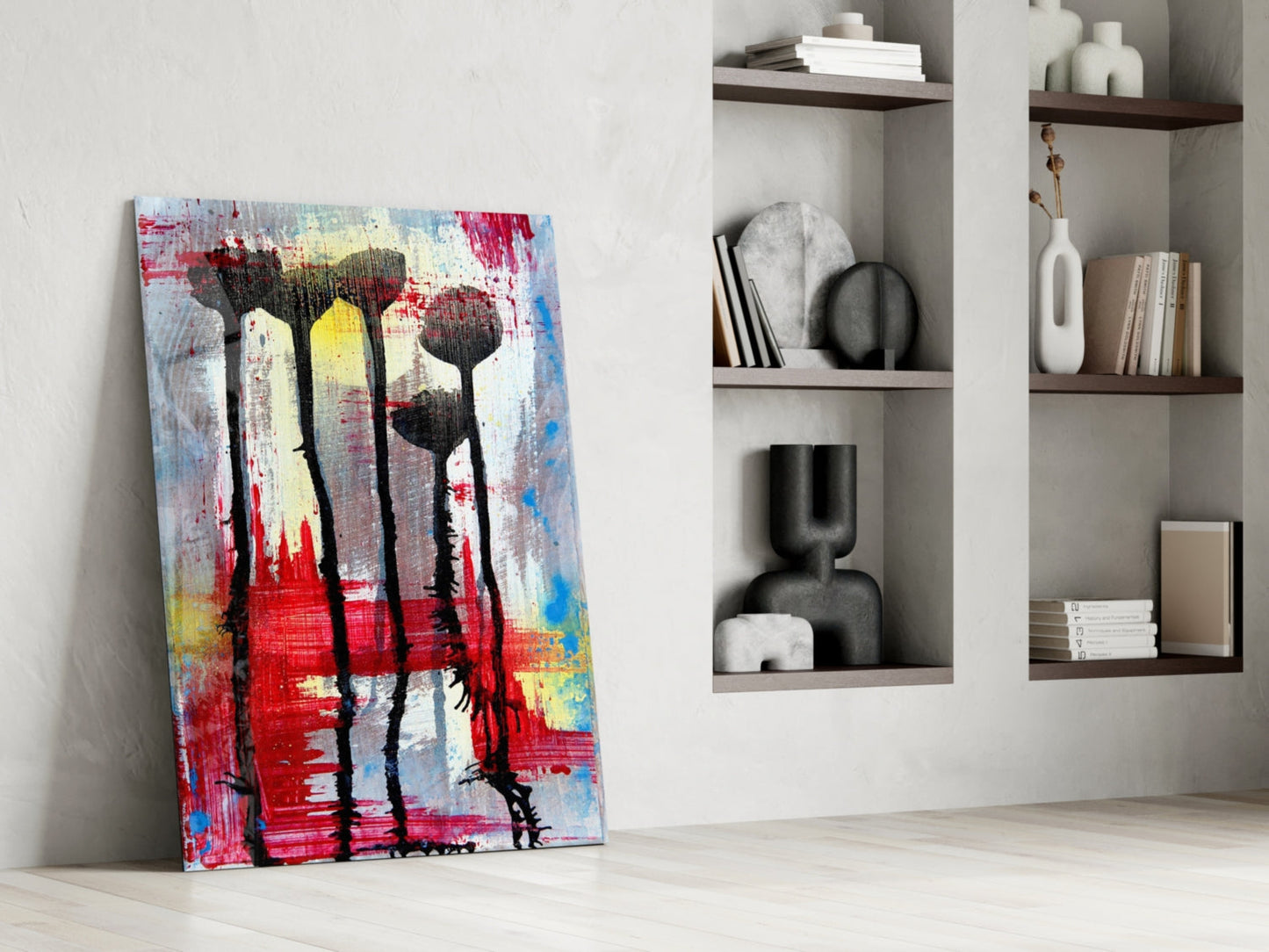 Colorful abstract glass art with black flower silhouettes leaning against white wall beside white shelving unit.