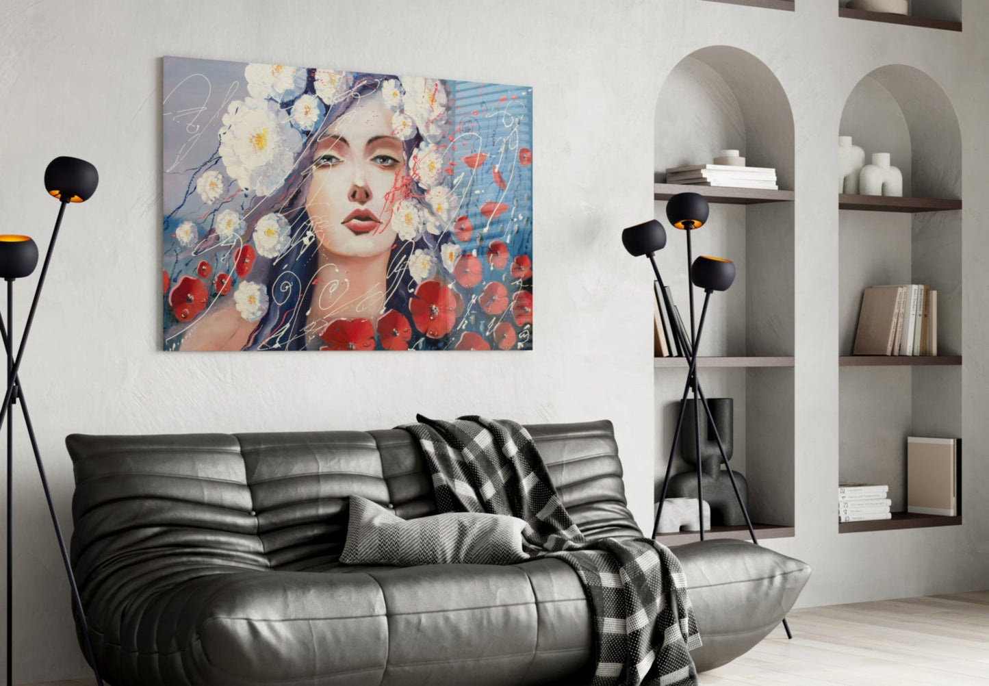 Modern living room with colorful glass wall art of woman's face surrounded by red and white flowers hanging above black leather sofa.