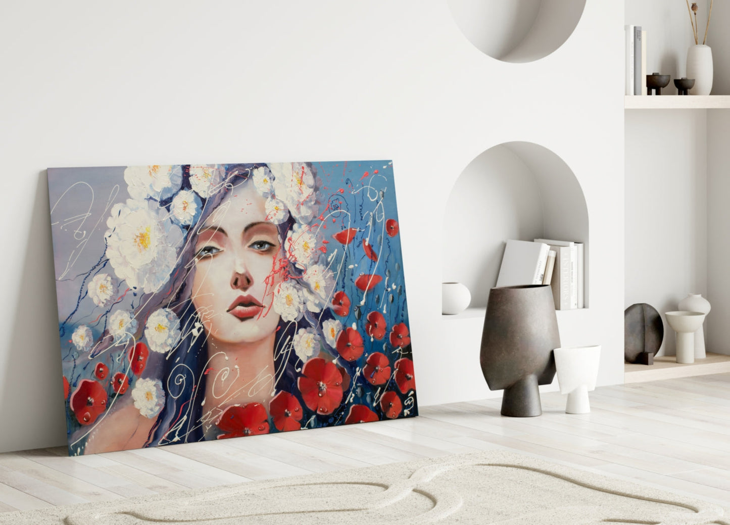 Modern minimalist interior displaying glass wall art of a woman's face surrounded by white daisies and red poppies against blue background, leaning against white wall near decorative objects.