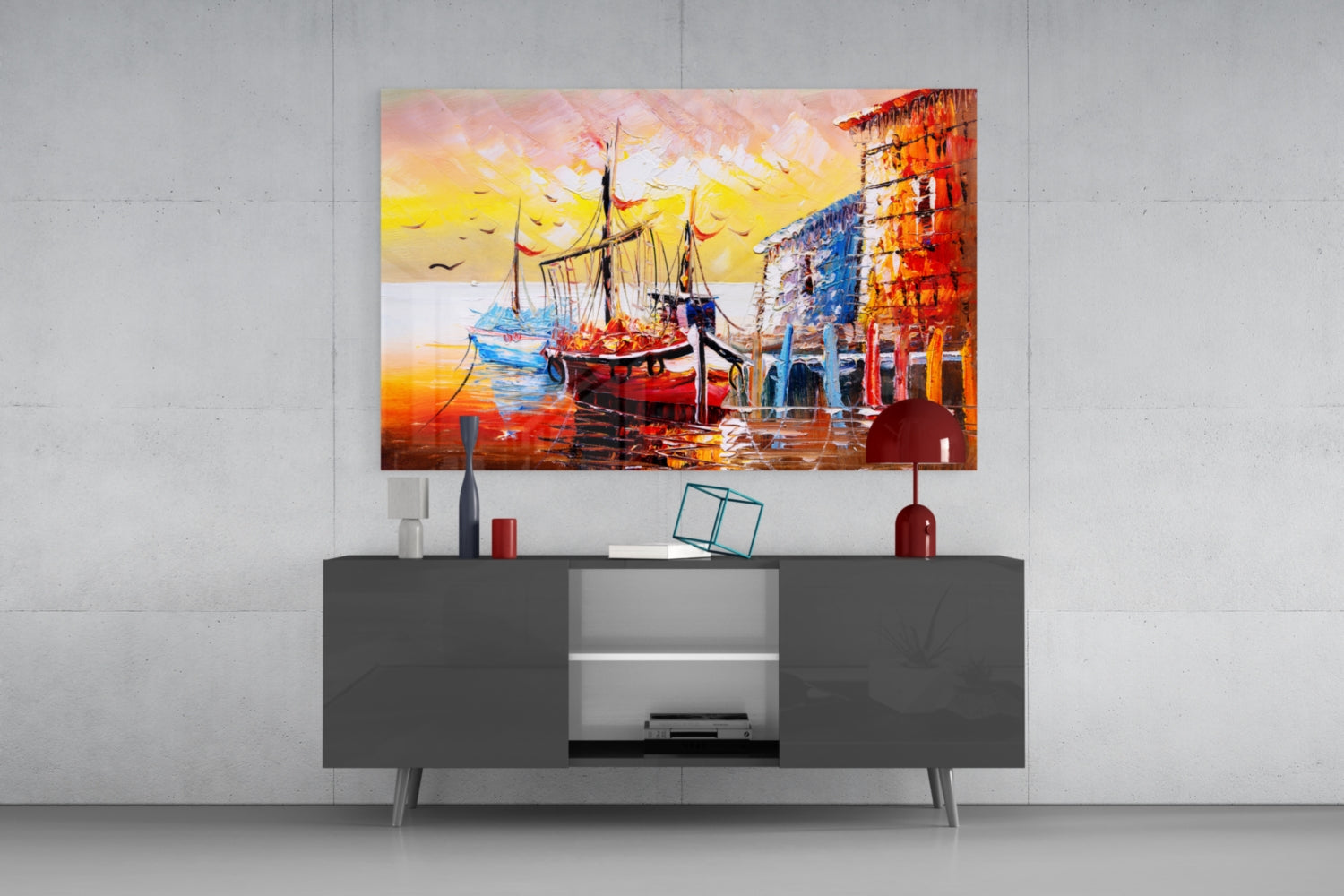 Glass wall art depicting sailboats at sunset harbor displayed above gray media console with decorative accessories.