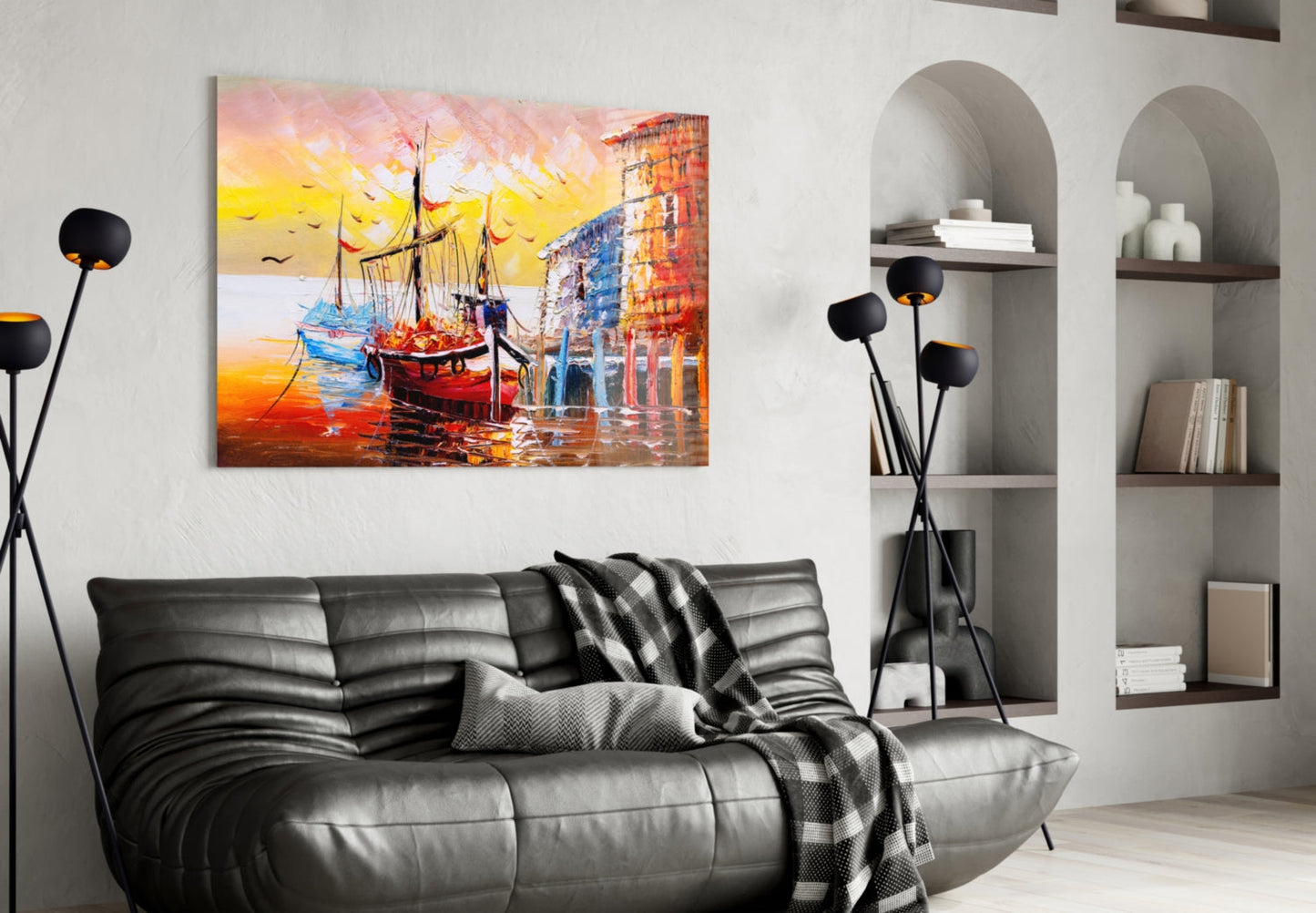 Colorful glass wall art depicting sailing ships at sunset displayed above a black leather sofa in a modern living room.