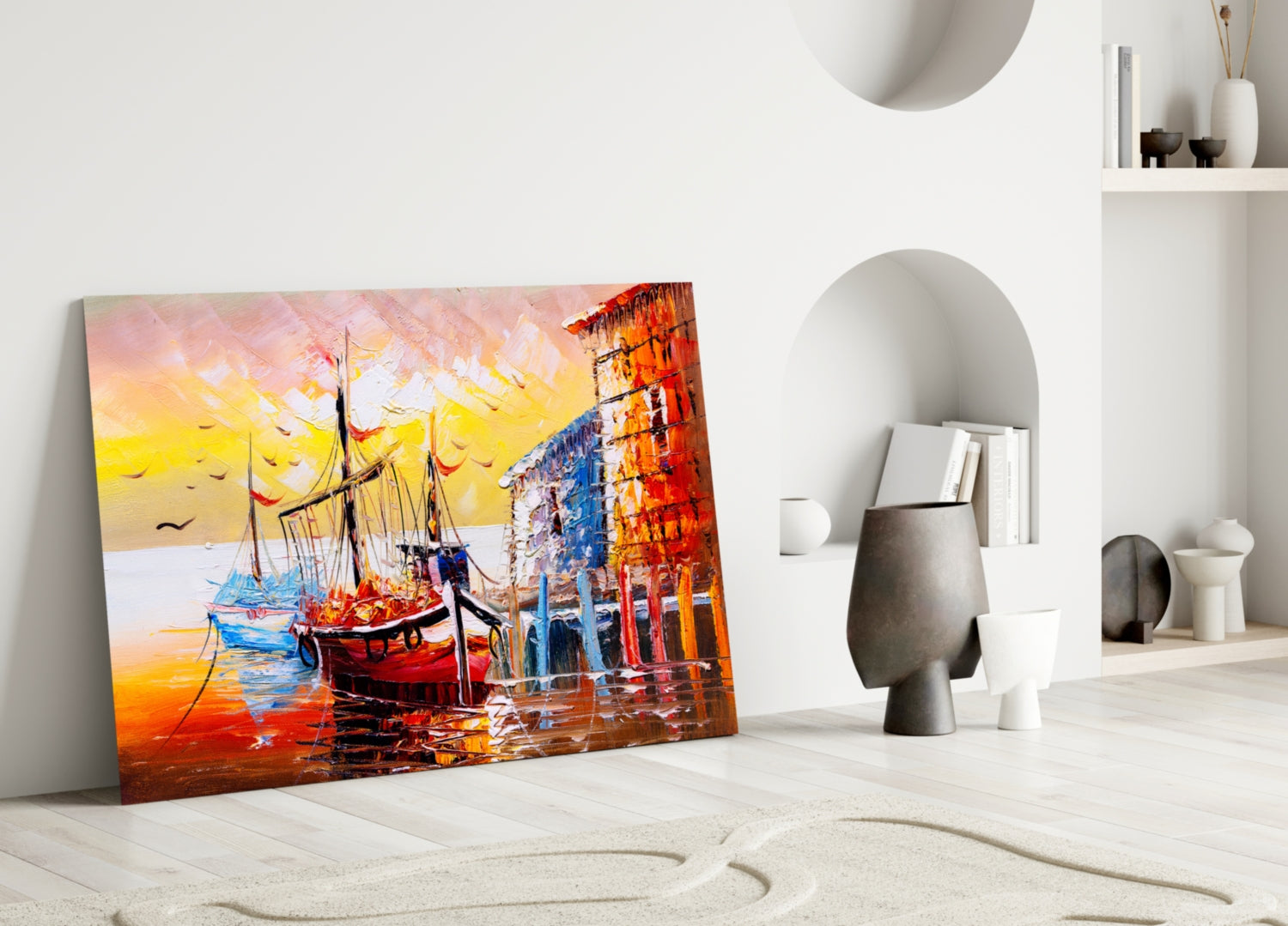 Colorful glass wall art depicting red sailing ships at sunset displayed leaning against white interior wall with decorative objects.