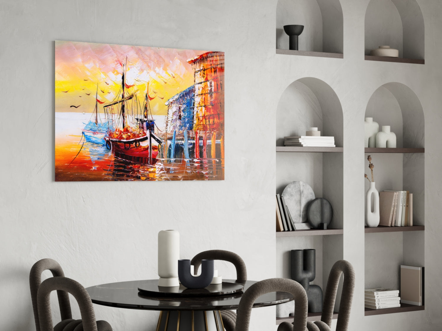 Colorful glass wall art depicting ships at sunset displayed above a round dining table in a modern interior.
