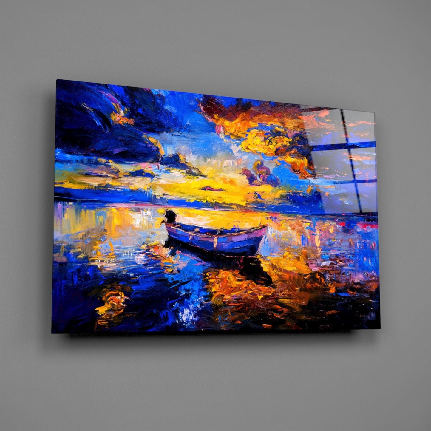Dark blue glass wall art depicting a lone boat on water at sunset with vibrant orange and yellow sky reflections, displayed at an angle on gray wall.