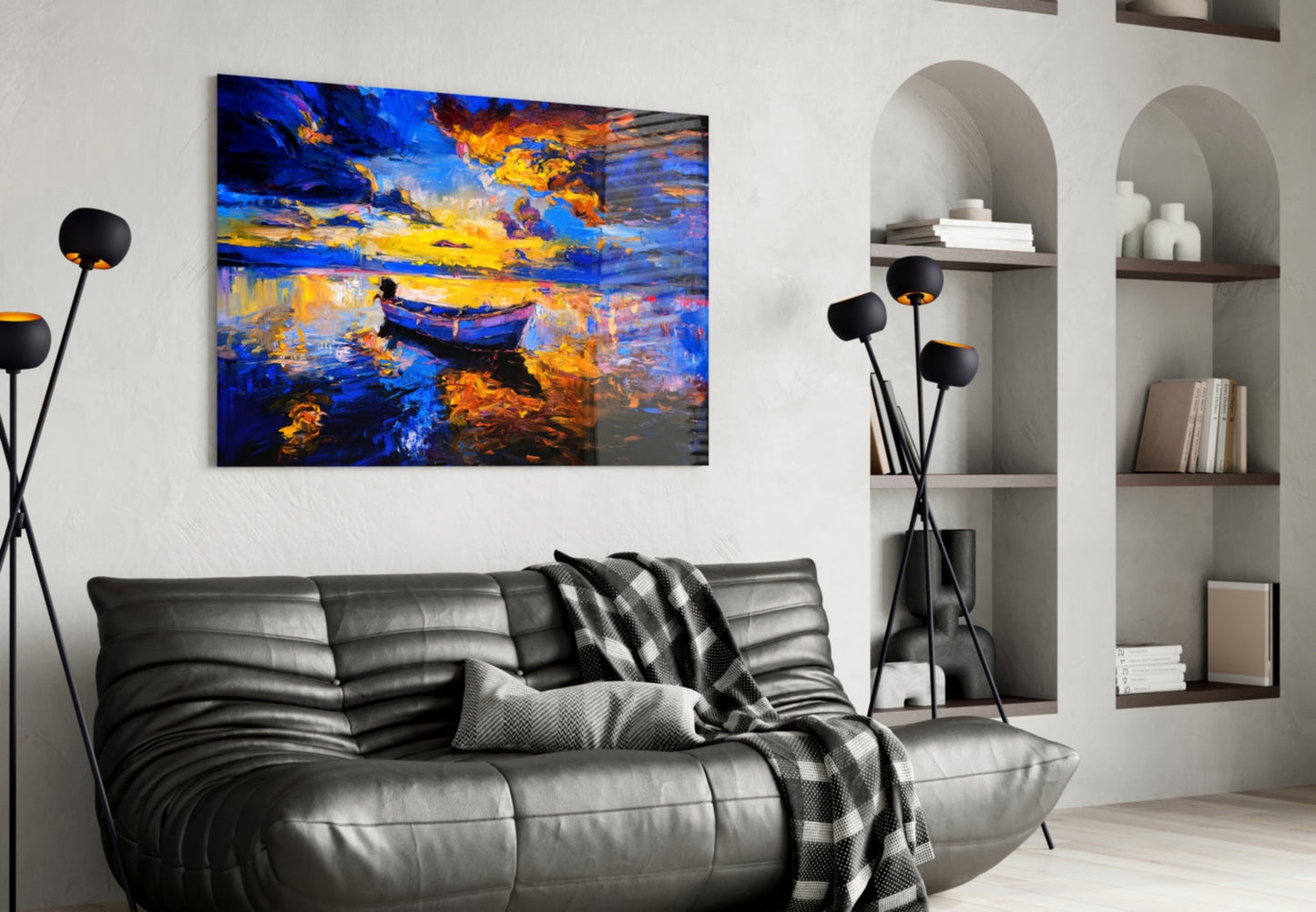 Dark blue sunset glass wall art depicting a golden-lit boat on water, displayed above a black leather sofa in a modern living room.