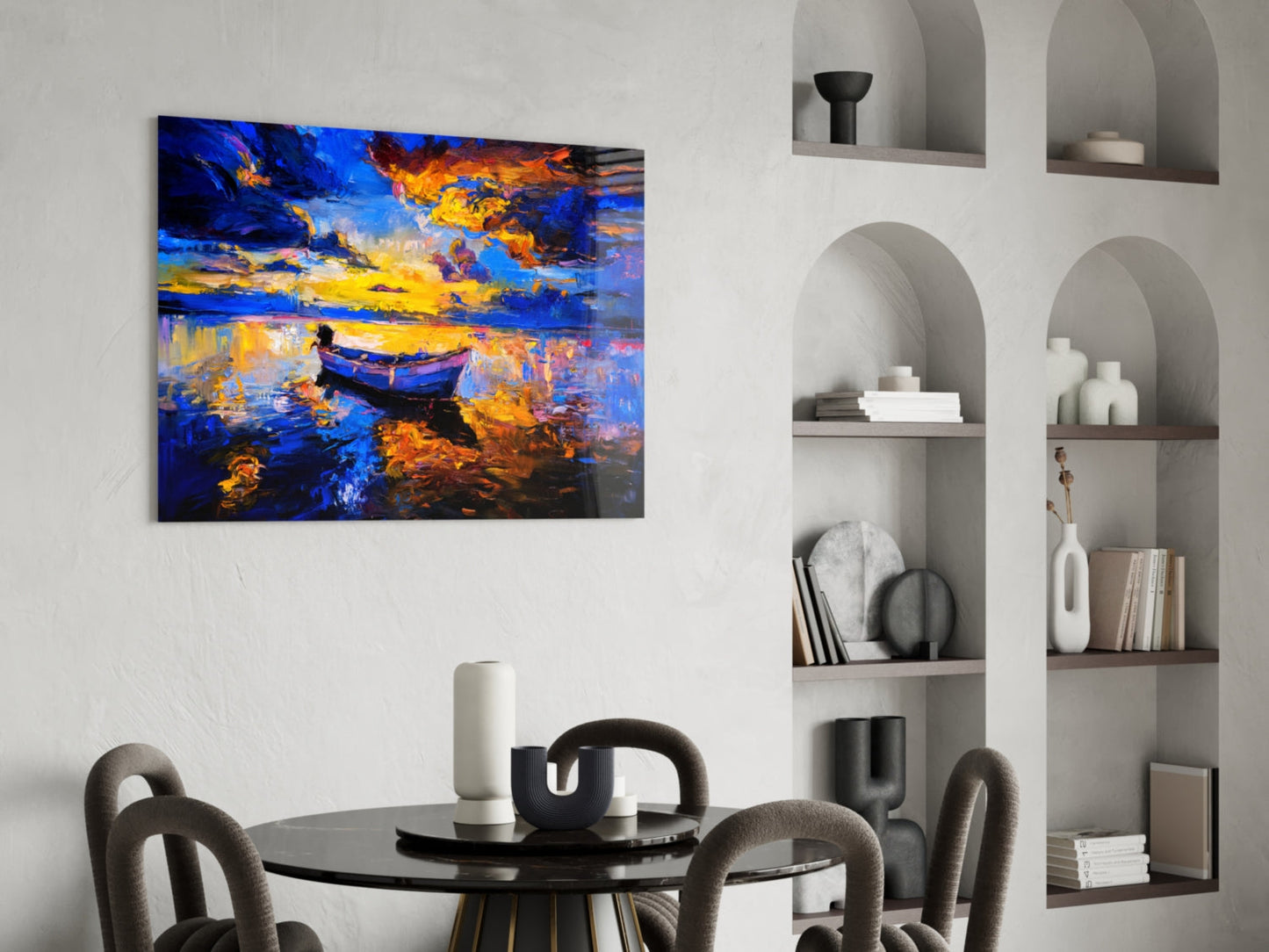 Dark blue glass wall art depicting a golden-lit boat on water, displayed above a round black dining table with modern chairs in a minimalist interior.