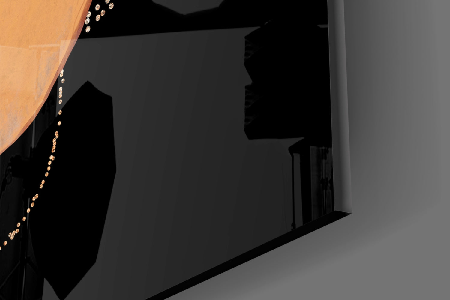 Black glass wall art panel mounted on gray wall with decorative gold beaded chain accent detail, angled interior view.