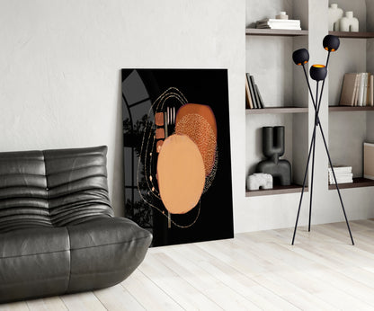 Abstract black glass wall art with terracotta and gold circular design displayed in modern living room with gray sofa and shelving.