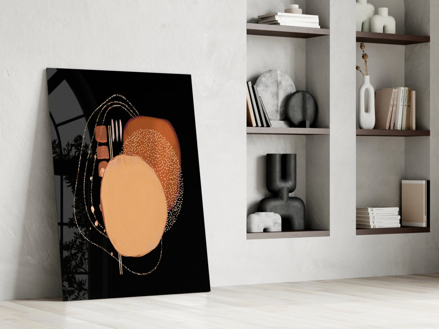 Abstract black glass wall art with orange and tan circular design leaning against white wall beside shelving.