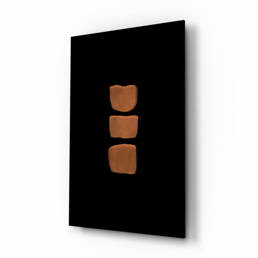 Black glass panel with three stacked terracotta-colored rounded square shapes arranged vertically in center, photographed at angled perspective.