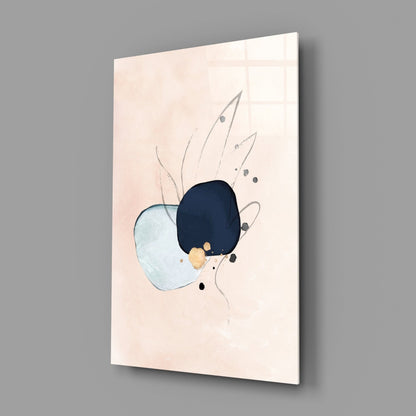 Angled view of glass wall art displaying abstract shapes in light blue, dark navy, gold, and black on cream background, mounted on gray wall.