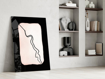 Modern minimalist glass wall art with black frame and cream-colored abstract line drawing, displayed against white wall with wooden shelving.
