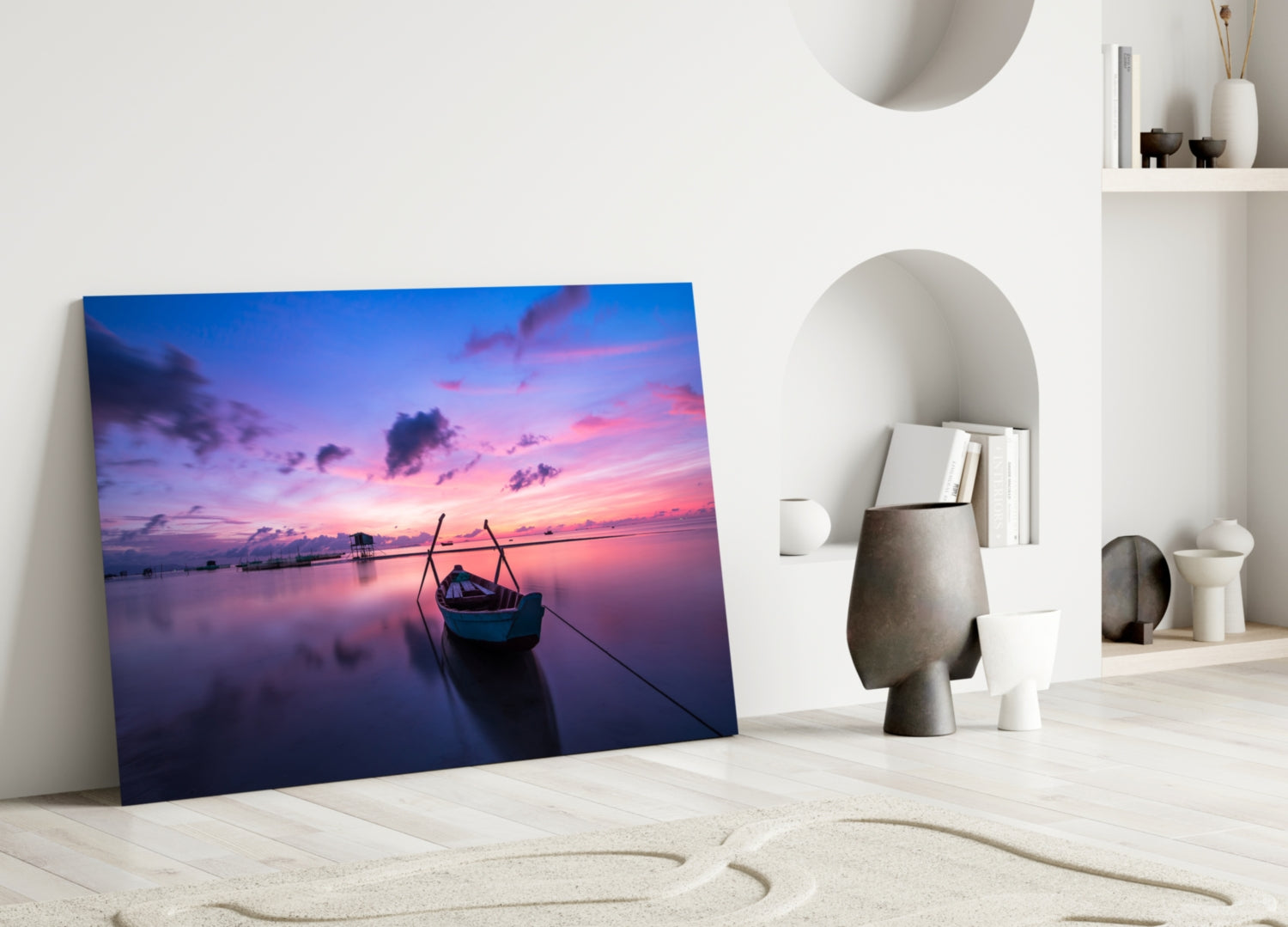Glass wall art leaning against white wall displays purple and pink sunset over calm water with silhouetted boat.