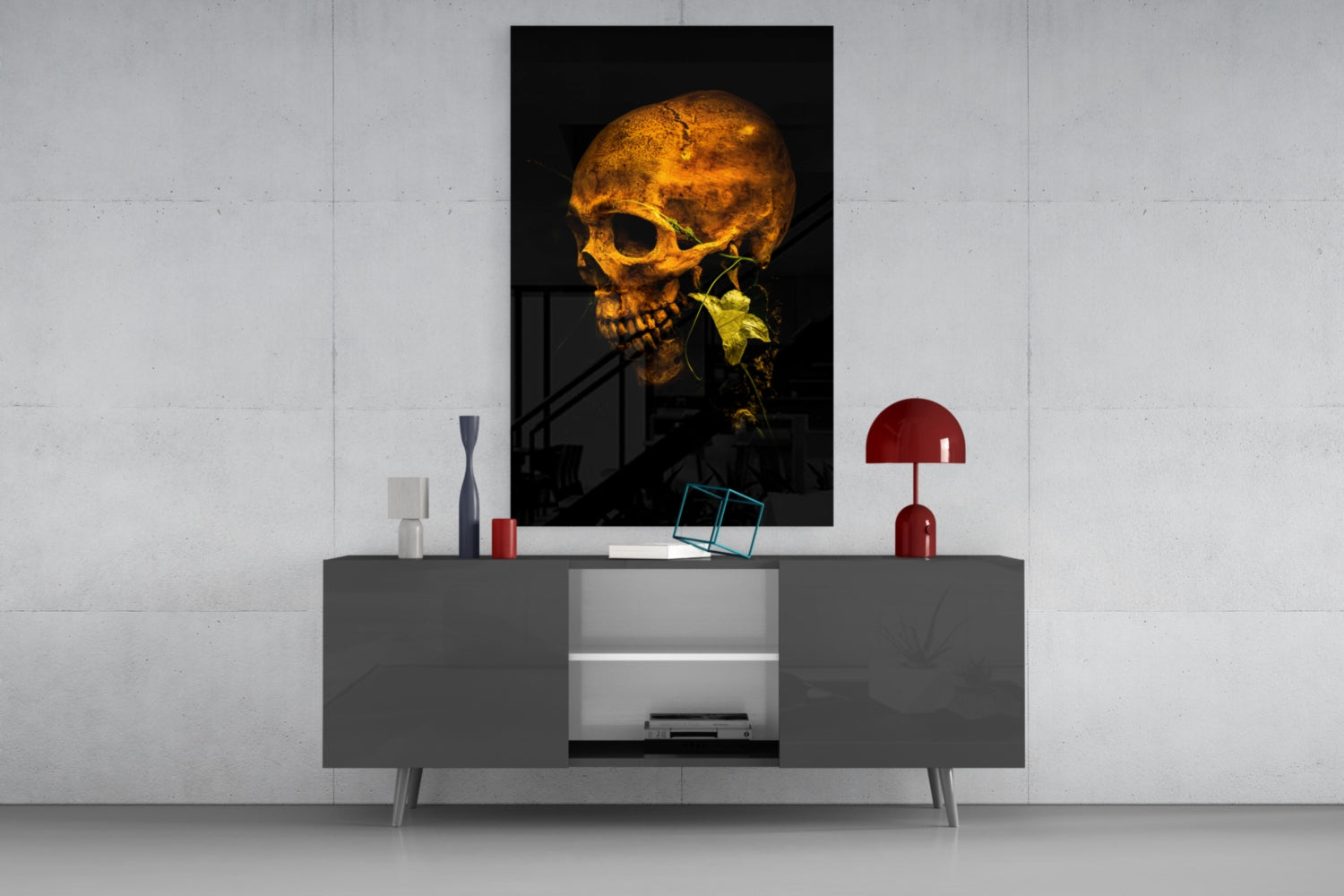 Golden skull with green plant stem in mouth displayed on wall above gray console table with red lamp and decorative objects.