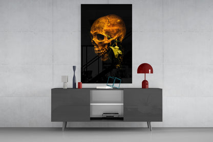 Golden skull with green plant stem in mouth displayed on wall above gray console table with red lamp and decorative objects.