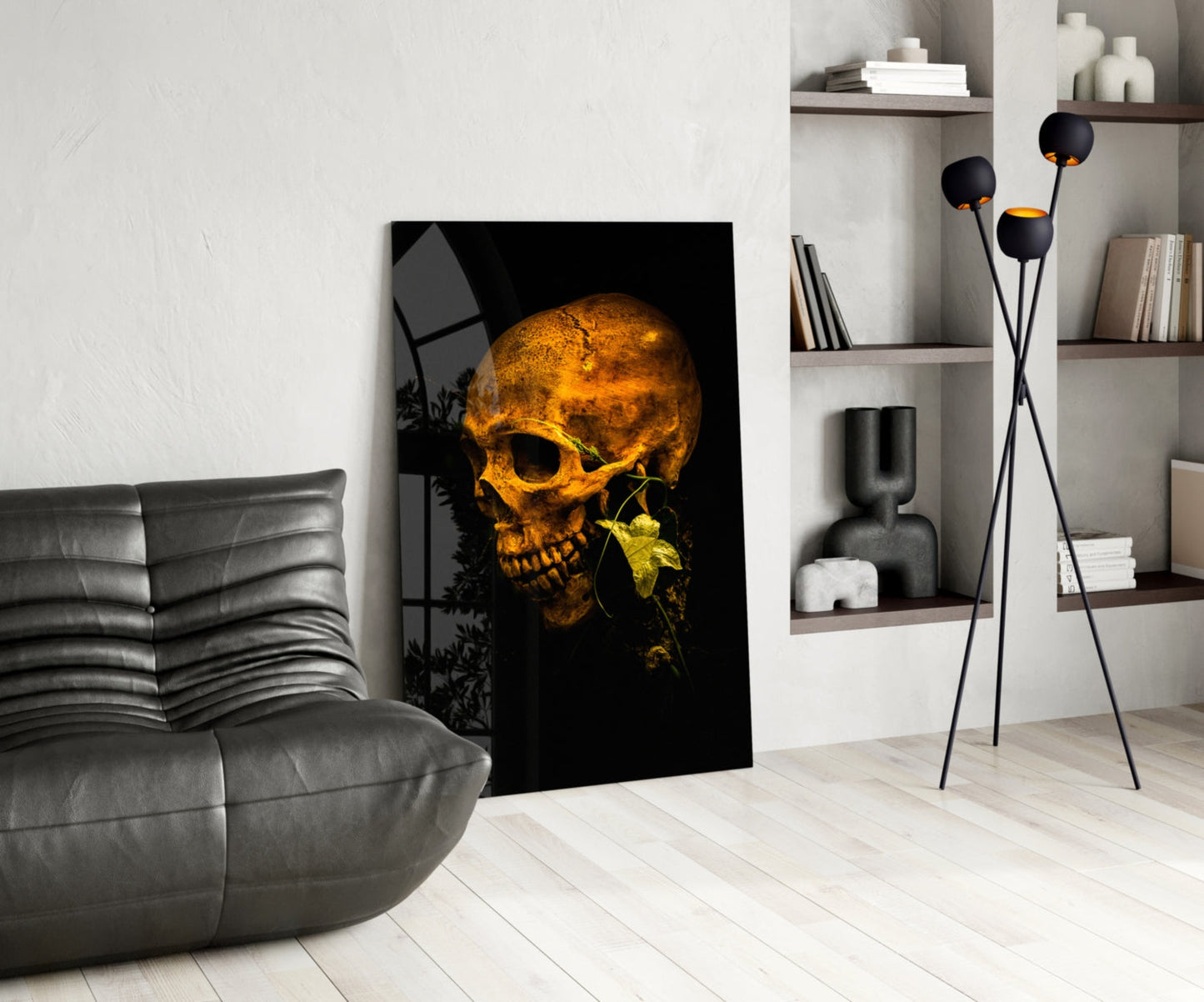 Golden glowing skull with green leaf on black glass art displayed in modern living room with gray sofa and shelving.