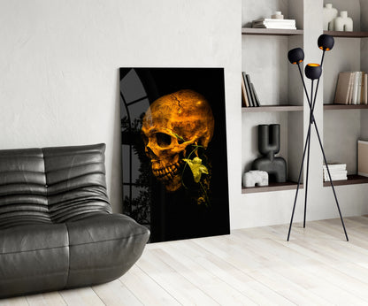 Golden glowing skull with green leaf on black glass art displayed in modern living room with gray sofa and shelving.