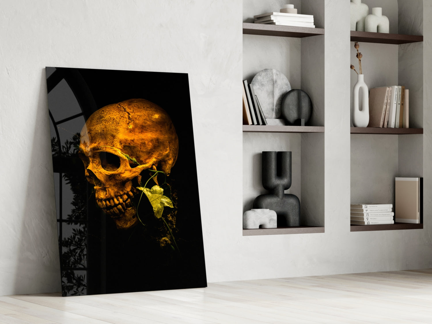 Golden skull with yellow flower on black background glass art leaning against white wall beside shelving.