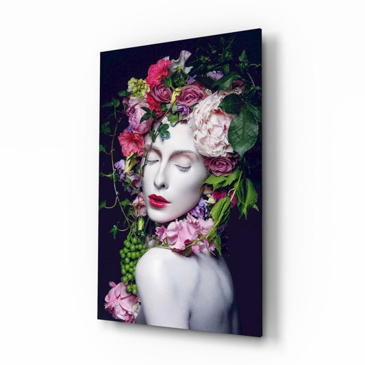 A woman's pale face with closed eyes and red lips adorned with pink, red, and white flowers against a dark background on glass.