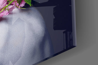 Close-up angled view of textured glass surface with pink flowers and green stems visible at top edge against white and dark background.