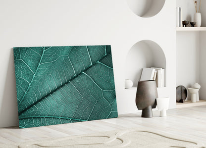 Teal glass wall art with detailed leaf vein texture leaning against white wall in minimalist interior setting.