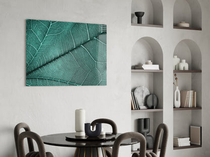 Teal leaf texture glass wall art hanging above a black round dining table with gray upholstered chairs and white shelving unit.