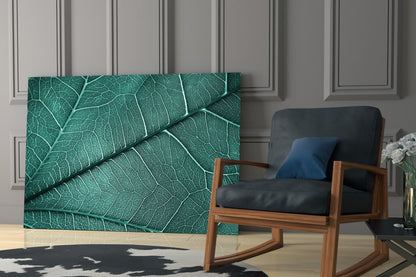 Teal leaf texture glass wall art displayed in a modern living room beside a wooden-framed chair with black leather cushions.