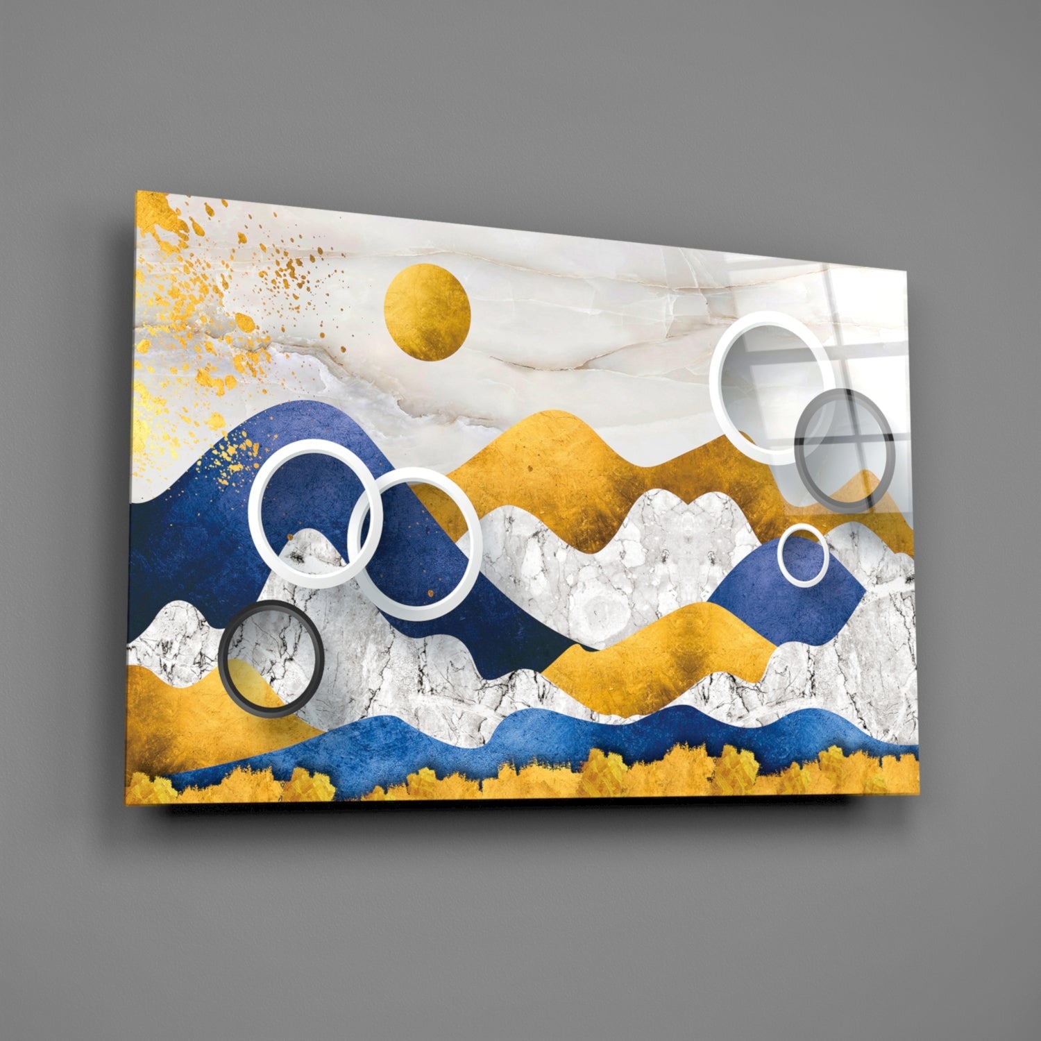 Angled view of glass wall art featuring layered mountains in gold, navy, and white with circular overlays against gray background.