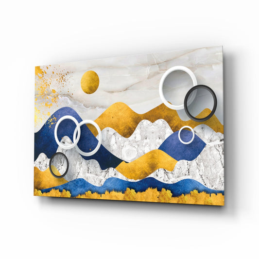 Modern glass wall art featuring layered abstract mountains in gold, navy blue, and white with overlapping circular rings, displayed at an angle.